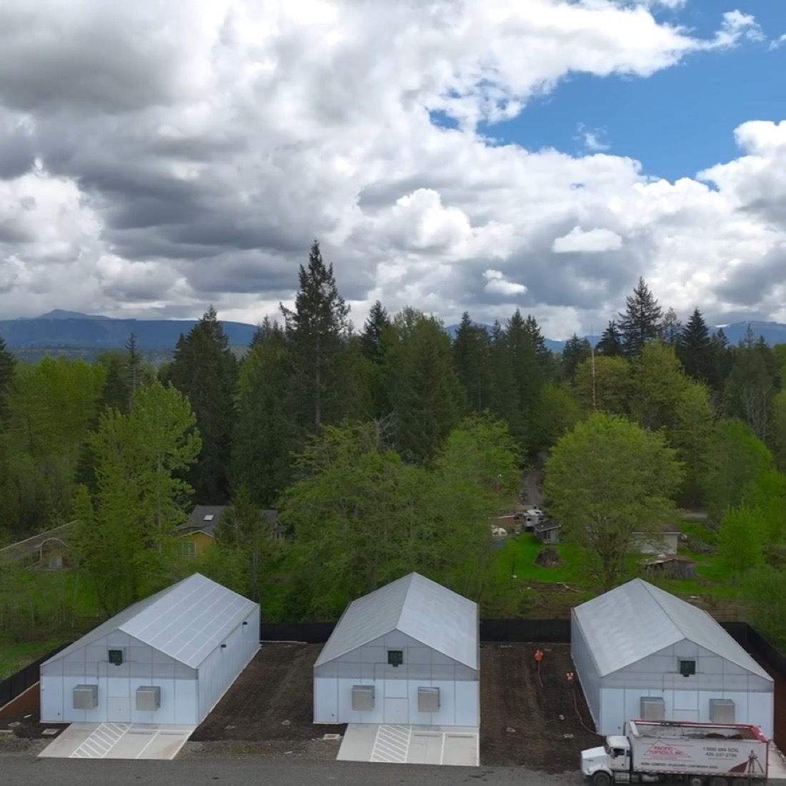 Aerial view of the 1937 Farms compound in Duvall — greenhouses, processing buildings and the red barn, surrounded by evergreen forest.
